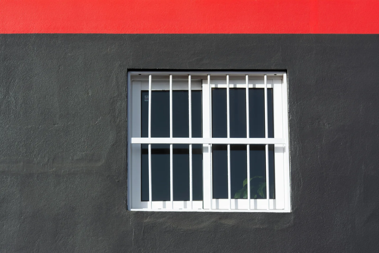 Barred residential window on a dark exterior wall with a red accent band, the kind of single-window opening common on Broward homes evaluating impact upgrades