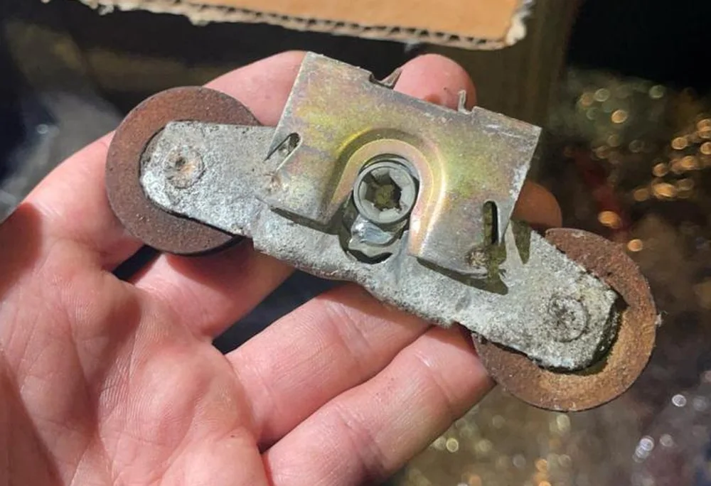 A worn tandem roller from a sliding patio door held in a hand, with a box of new rollers behind it